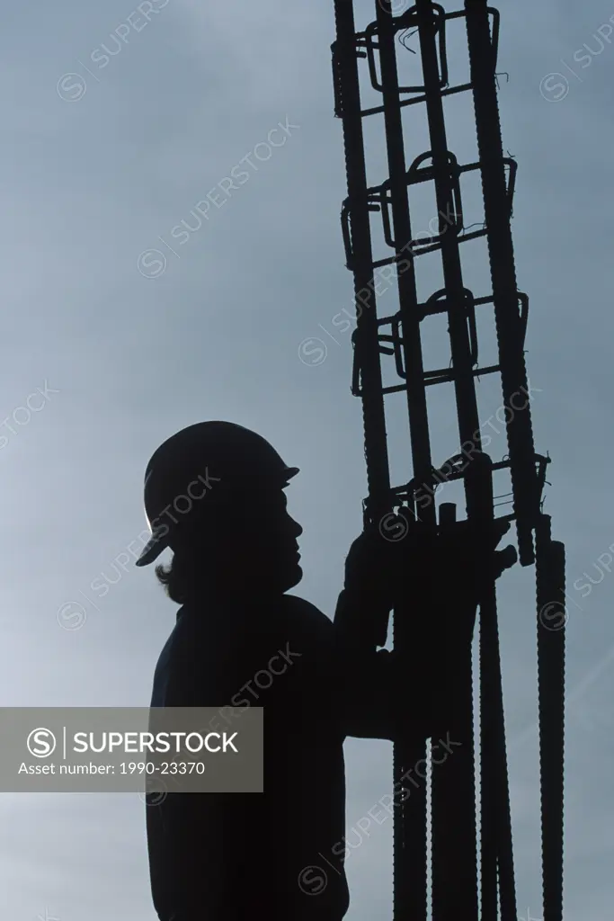 Steelworker in sillouette while tying steel in column on construction site with hardhat, British Columbia, Canada