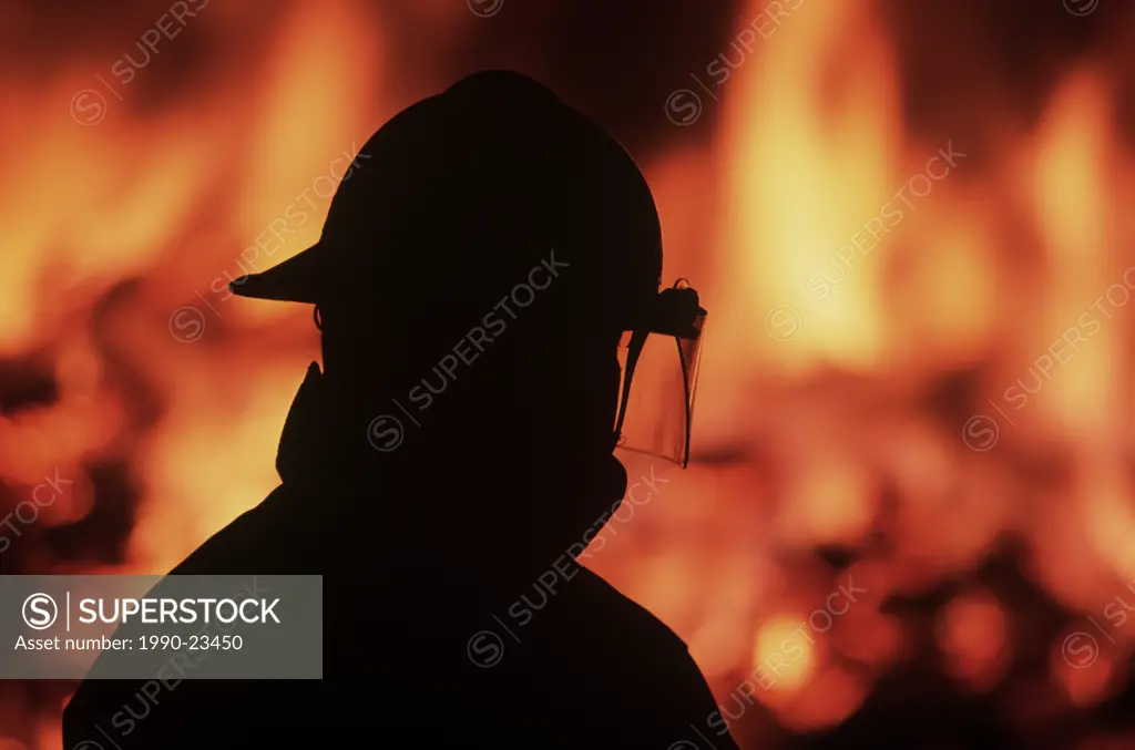 Silhouette of fireman with burning house beyond, British Columbia, Canada