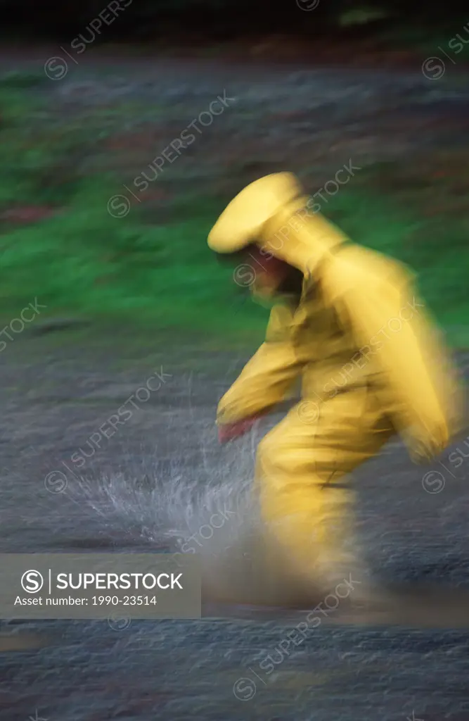 Boy in yellow raincoat kicks mud puddle, motion blur, British Columbia, Canada