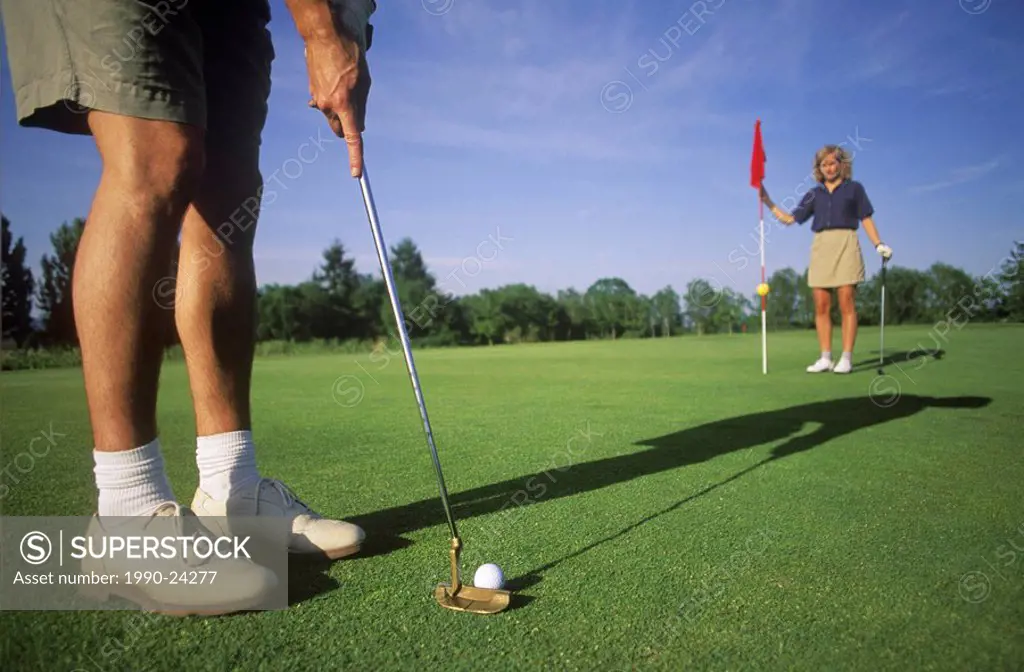 male golfer lines up put while female companion holds flagstick, British Columbia, Canada