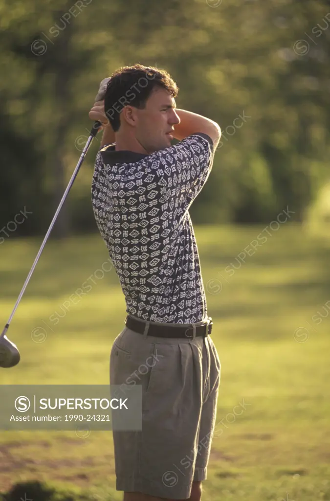 Male golfer watches drive, warm toned, British Columbia, Canada
