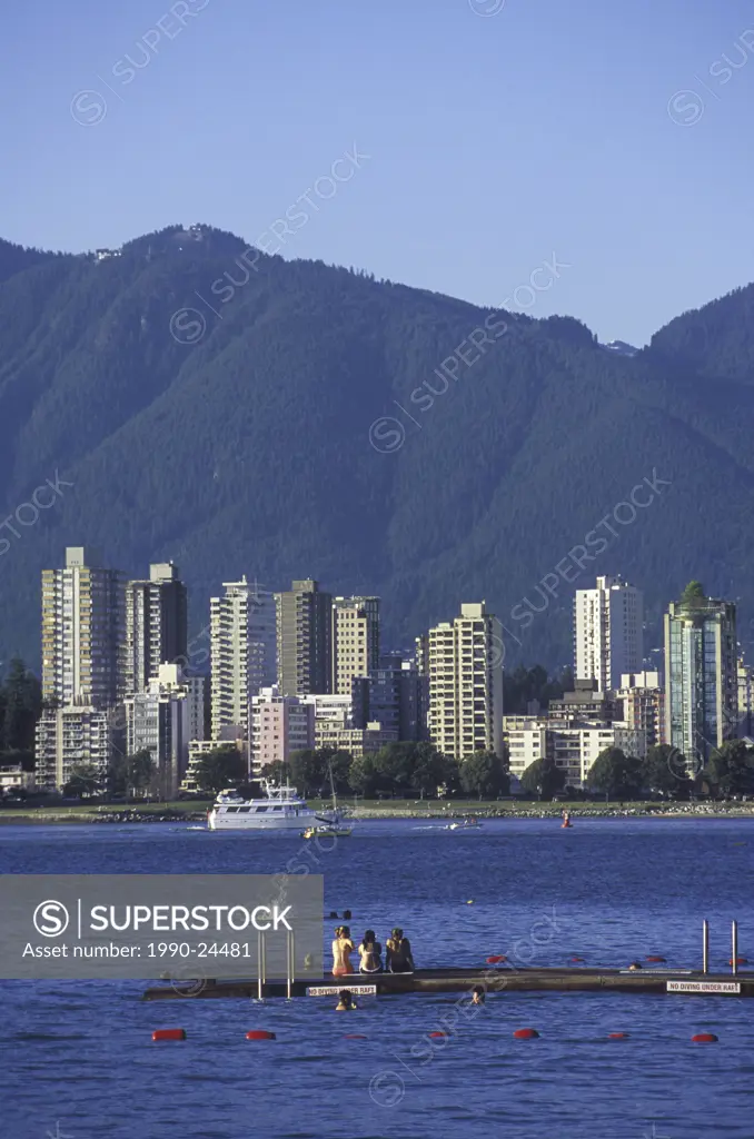 Teens play on a dock in English Bay along Kitsilano Beach, downtown Vancouver beyond, Vancouver, British Columbia, Canada