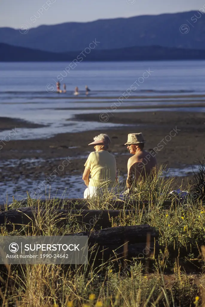 Parksville Beach Older couple sits on log at beach, Vancouver Island, British Columbia, Canada