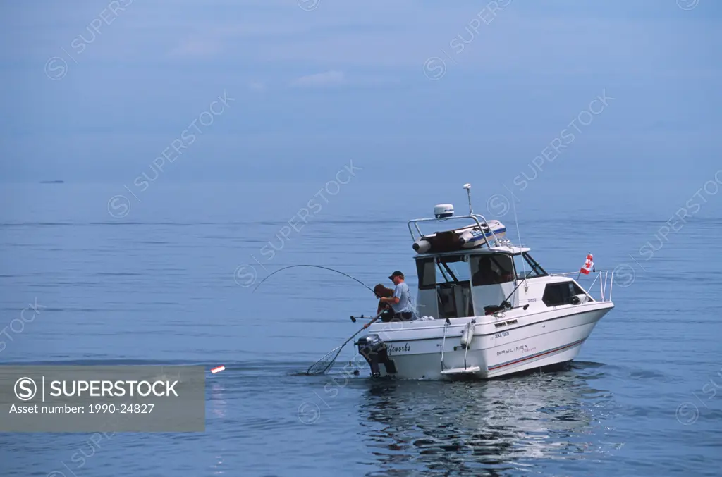 Two men playing salmon on small fishing boat, Vancouver Island, British Columbia, Canada