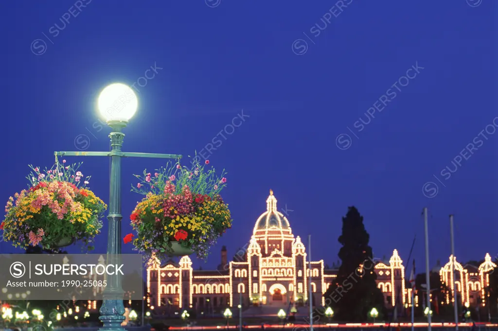 Flower baskets hanging from lamp posts with the Parliament buildings lit at night beyond, Victoria, Vancouver Island, British Columbia, Canada