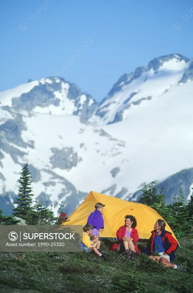 young family camps in meadow with mountain backdrop in Whistler Alpine, Whistler, British Columbia, Canada