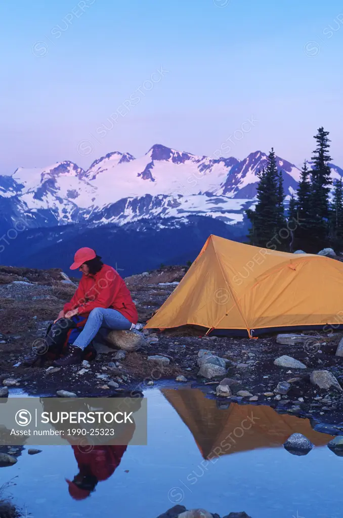 Woman camps in meadow with mountain backdrop in Whistler Alpine, Whistler, British Columbia, Canada