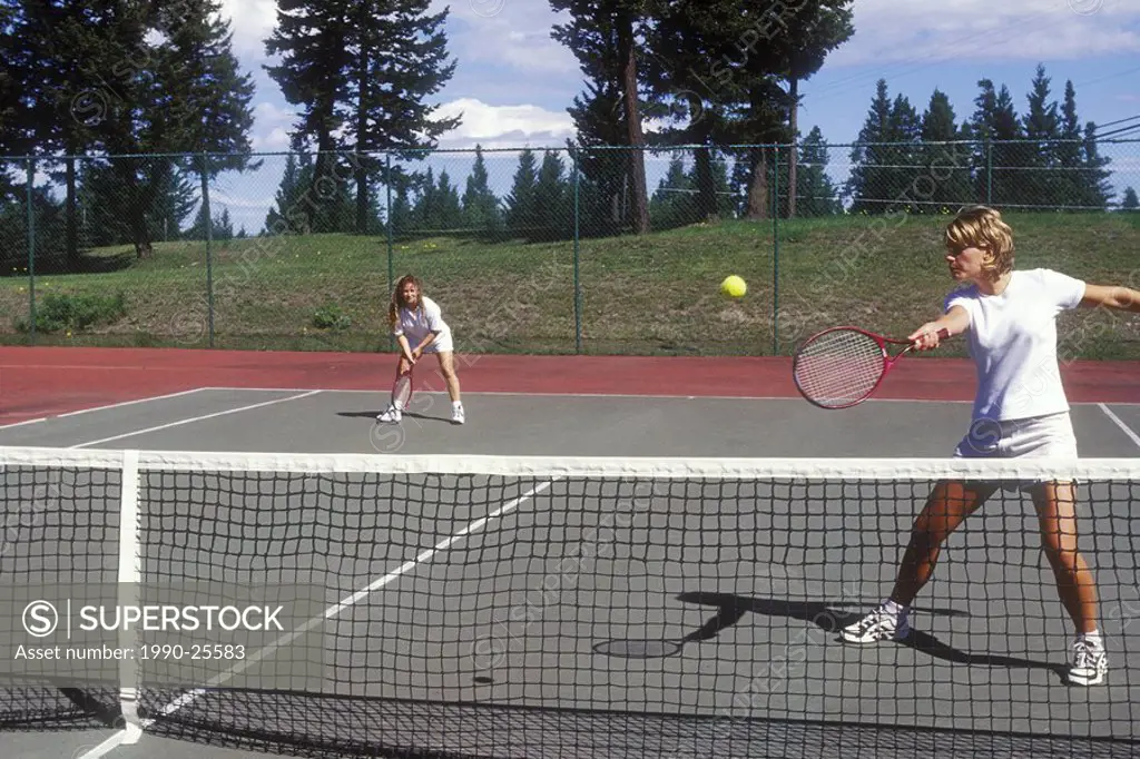 Two women playing doubles tennis, 108 Mile Rd, British Columbia, Canada