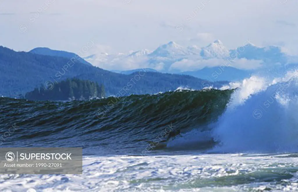 Surfer bottomturning with mountains beyond near Tofino, Vancouver Island, British Columbia, Canada