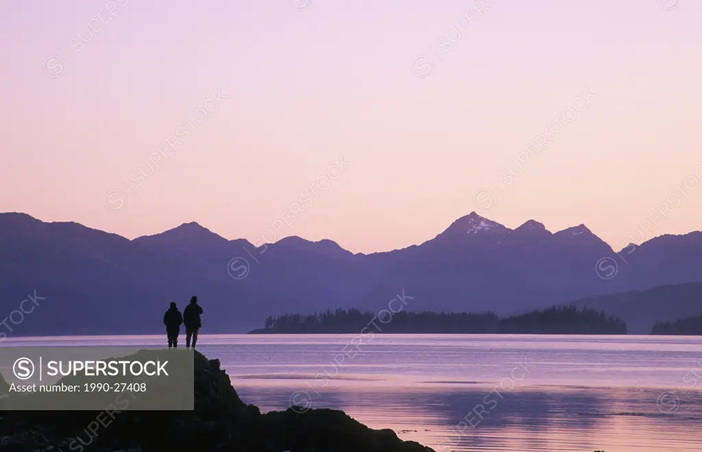 Couple watching a sunset over the San Cristoval Mountains, Queen Charlotte Islands, British Columbia, Canada