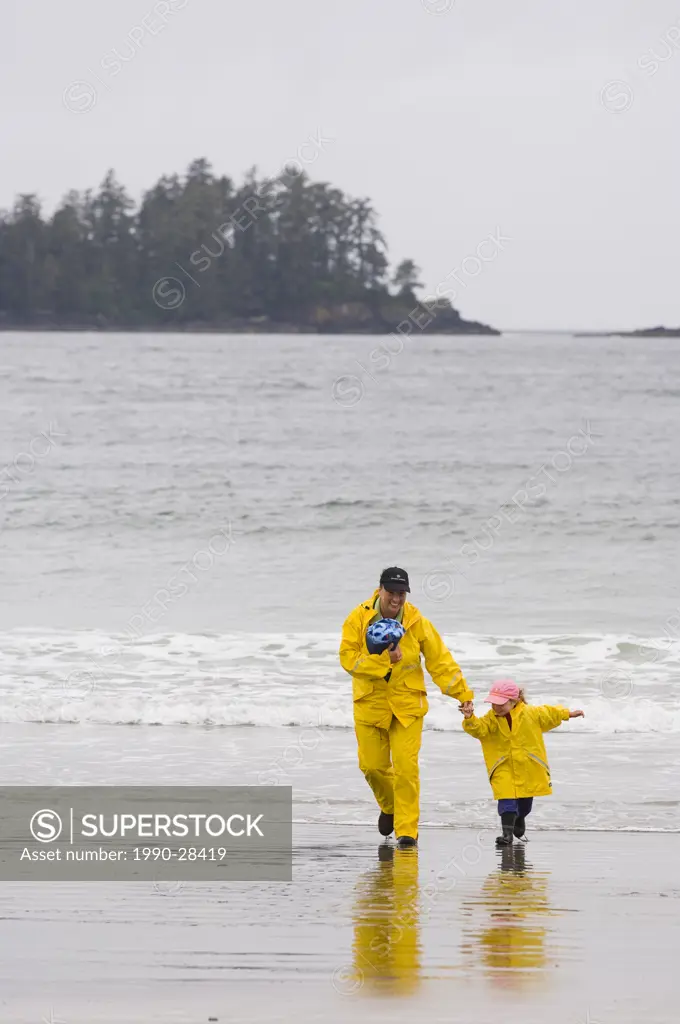 mother and daughter in yellow rain gear walk beach, MacKenzie Beach at Tofino, Vancouver Island, British Columbia, Canada
