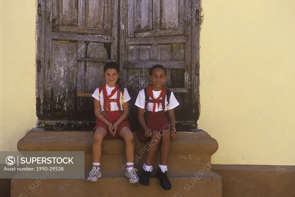 Cuba, Trinidad, two 10 year old girls in school uniform sit on steps to house