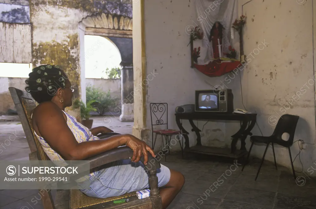 Cuba, Trinidad, woman watches Castro on television, Santeria effigy above TV