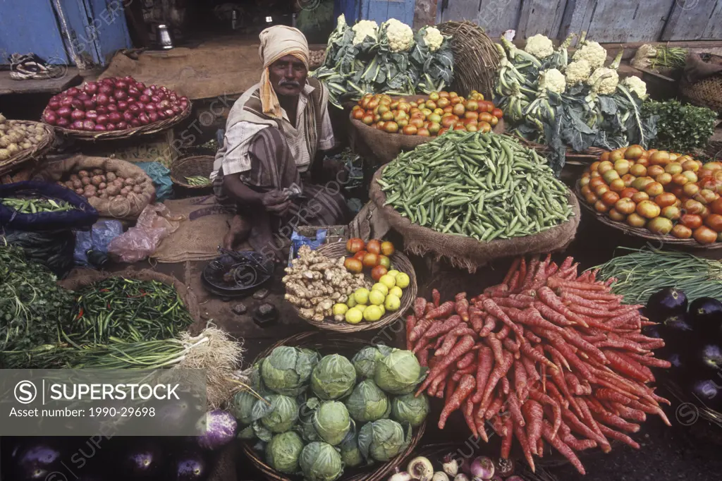 India, Varanasi, man selling vegetable produce at outdoor market.