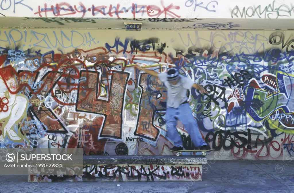 USA, Los Angeles, Vencie Beach _ Young skater rides skateboard in front of graffiti covered wall.