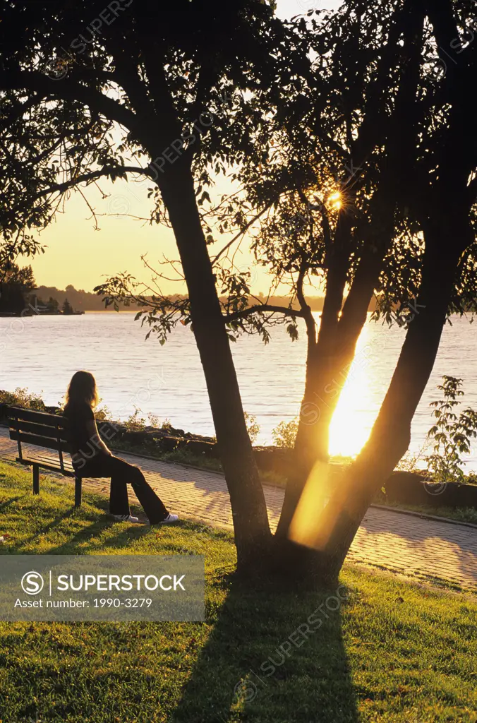 Young lady sitting on park bench in Bell Park near Ramsey lake at sunrise, sudbury, ontario, Canada