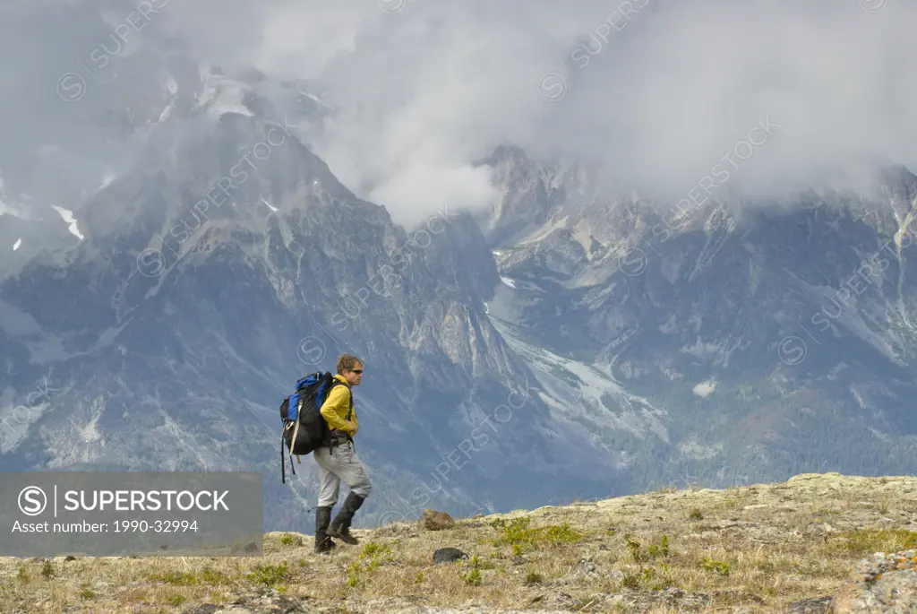 A hiker traverses a ridge in the Potato Range, with a foggy view of the Niut Range behind, British Columbia, Canada