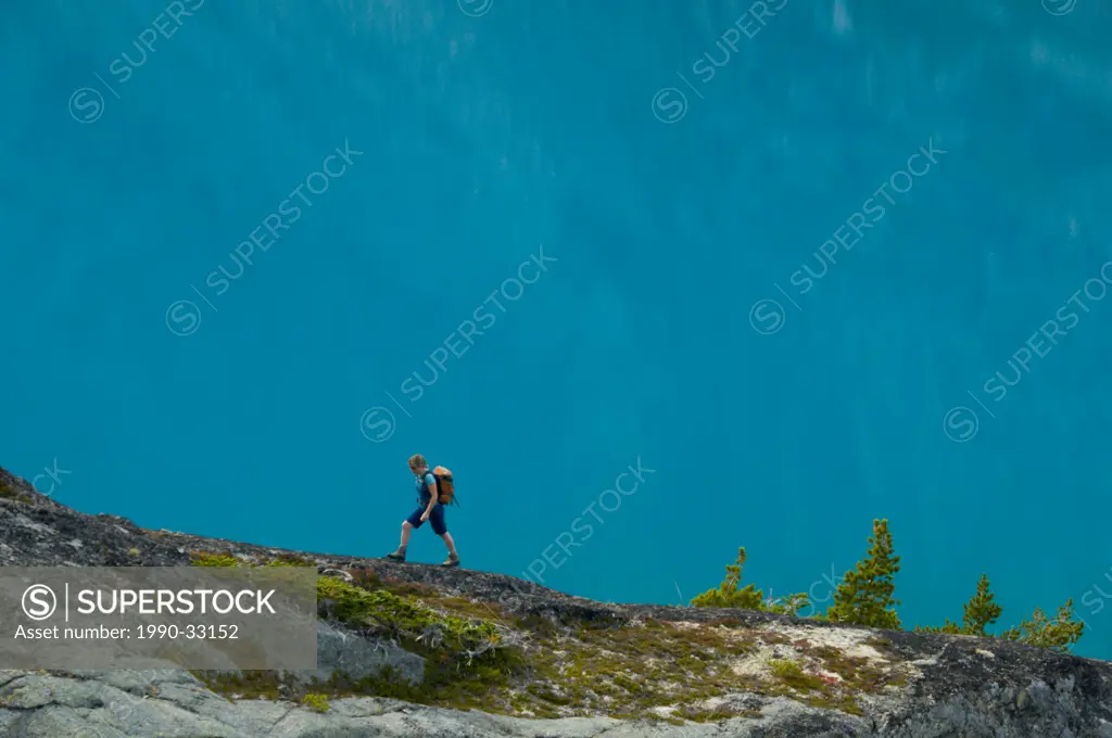 A young woman hikes in front of a blue lake in the Niut Range, British Columbia, Canada