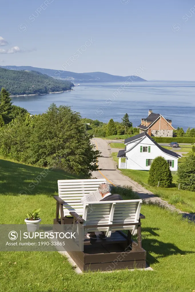 Elderly man reading a newspaper while seated on a glider and surrounded by a picturesque environment, Saint_Irenee, Quebec, Canada