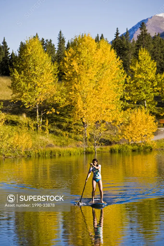 A young asian woman uses her paddle board on a small lake in Canmore, AB