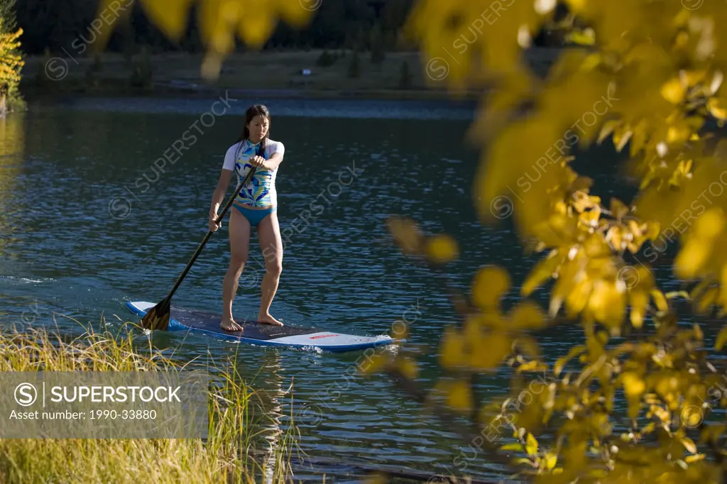A young asian woman uses her paddle board on a small lake in Canmore, AB