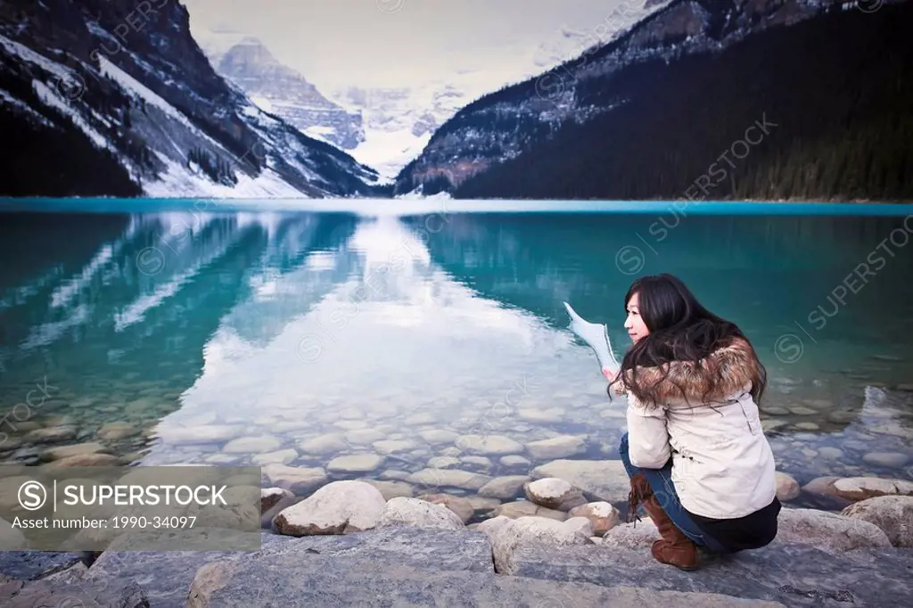 Young teenage girl tourist, holding up piece of ice from Lake Louise. Banff National Park, Alberta, Canada.