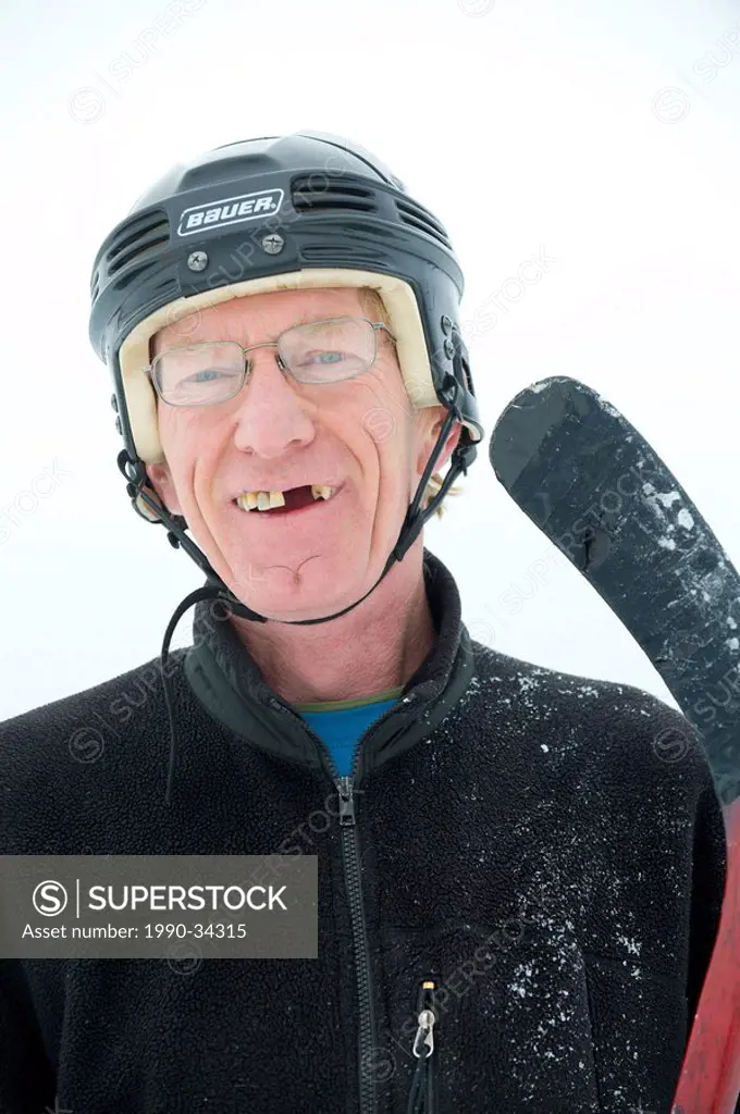 A happy hockey player with missing teeth and a stick smiles during a pond hockey game in Rossland, British Columbia, Canada