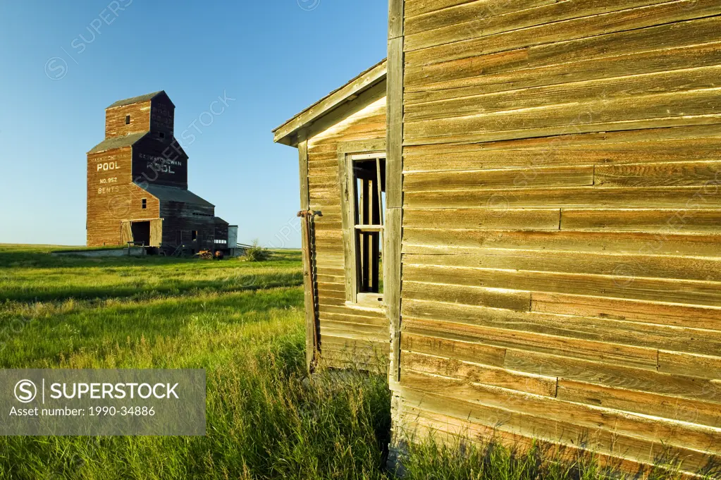 old house with grain elevator in the background, abandoned town of Bents, Saskatchewan, Canada