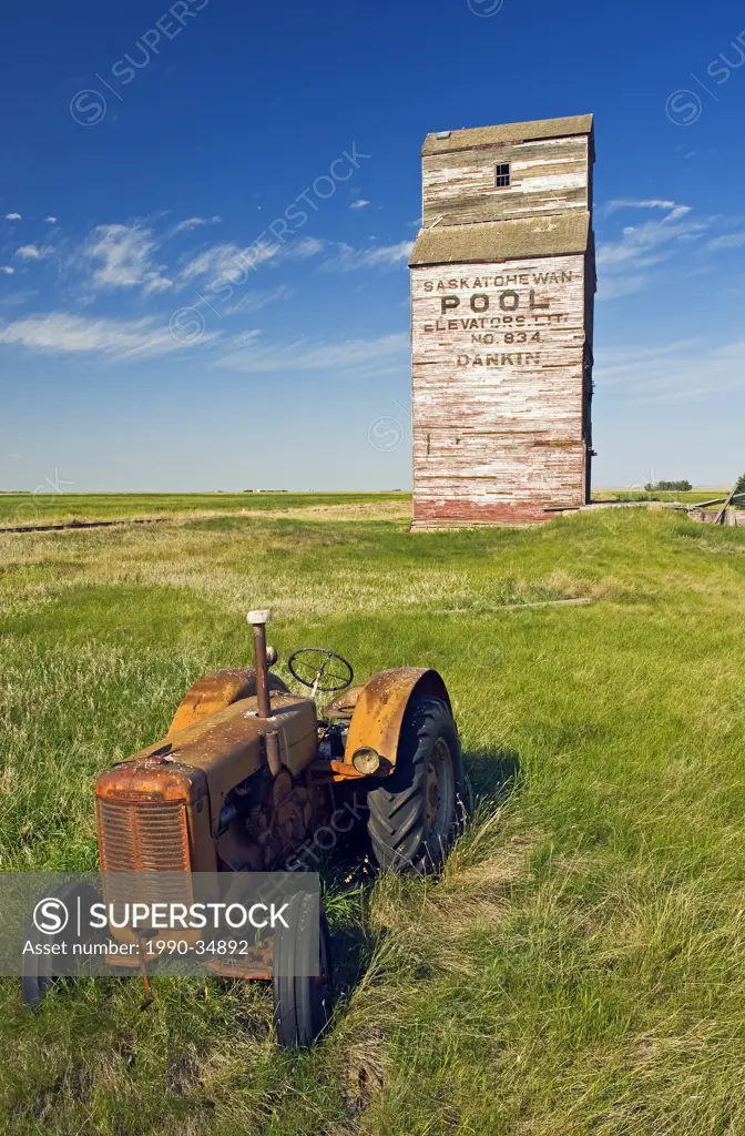 old tractor with abandoned elevator in the background, Dankin, Saskatchewan, Canada