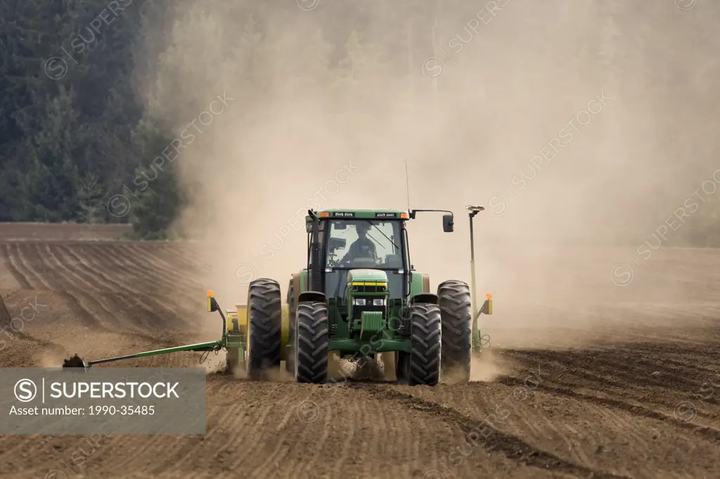 A farmer plants corn and fertilizes at the same time as his tractor maintains a straight and steady row. Courtenay, The Comox Valley, Vancouver Island...