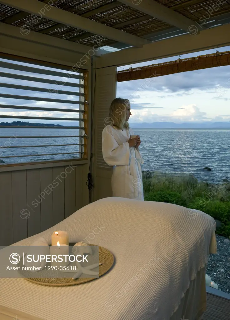 A young woman gazes out ot the Ocean in front of a beach front massage hut. Courtenay, The Comox Valley, Vancouver Island, British Columbia, Canada.