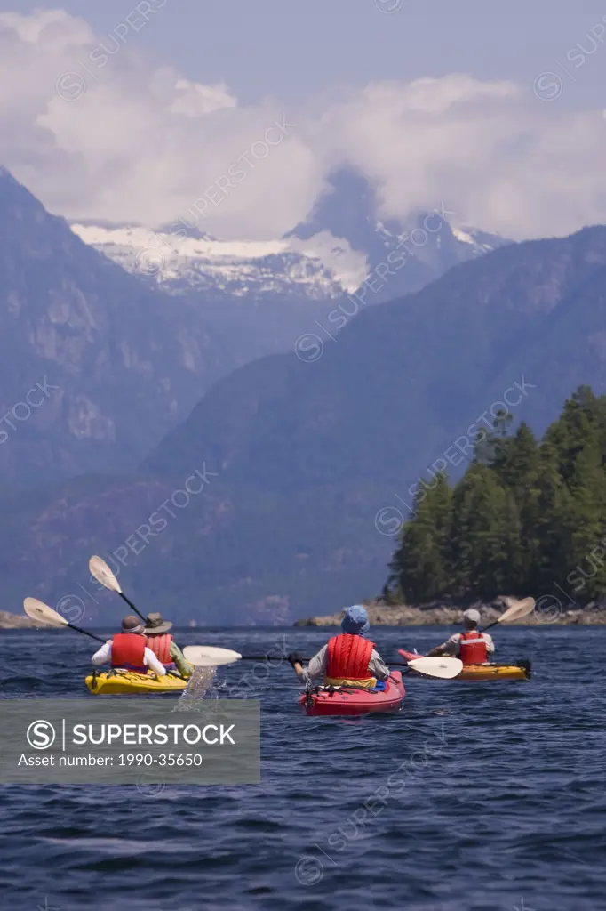 Kayakers paddle through Homfray Channel near Desolation Sound with Mount Denman cloaked in clouds rising into the background. Desolation Sound, Britis...
