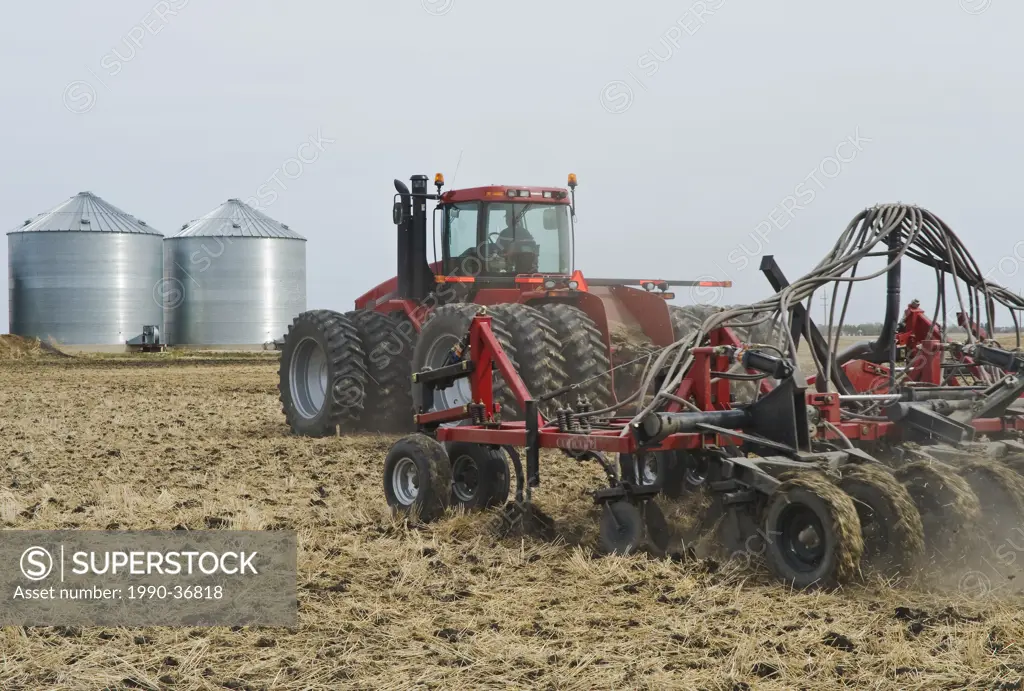 moving tractor and and air till seeder planting grain in canola stubble, near Dugald, Manitoba, Canada