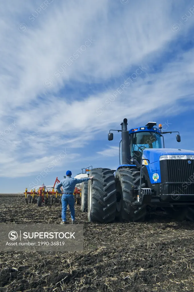 a man beside tractor and air till seeding equipment, near St. Agathe, Manitoba, Canada
