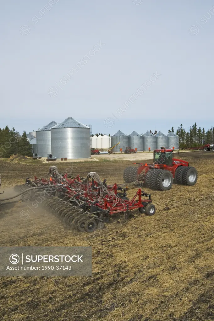 moving tractor and and air till seeder planting canola in wheat stubble, farmyard in the background, near Dugald, Manitoba, Canada
