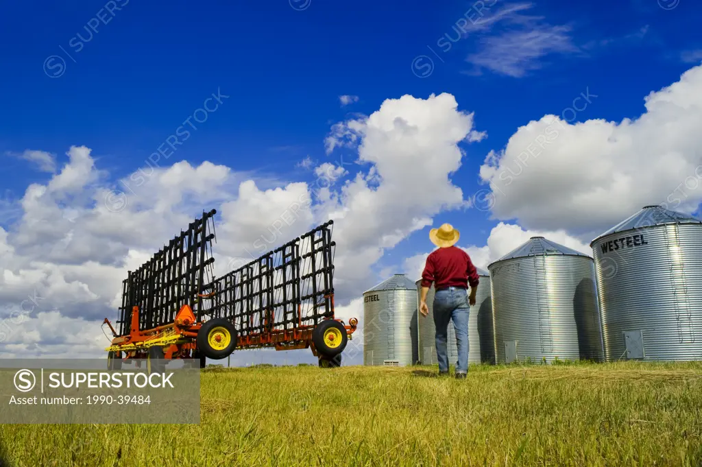a man lwalks towards harrowing equipment next to grain storage bins, near Carey, Manitoba ,Canada
