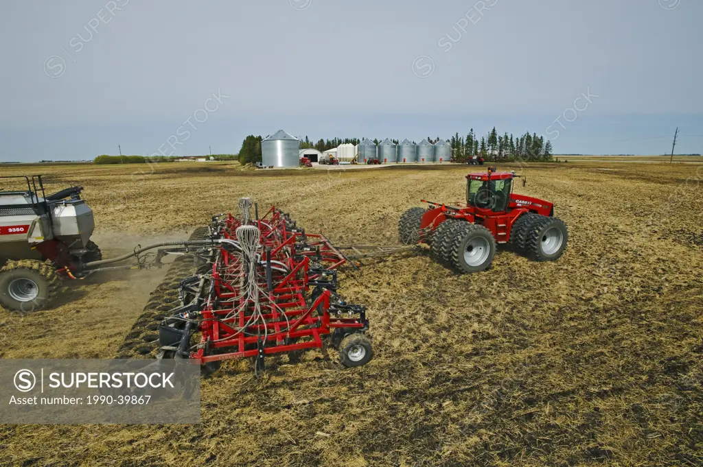 moving tractor and and air till seeder planting canola in wheat stubble, farmyard in the background, near Dugald, Manitoba, Canada