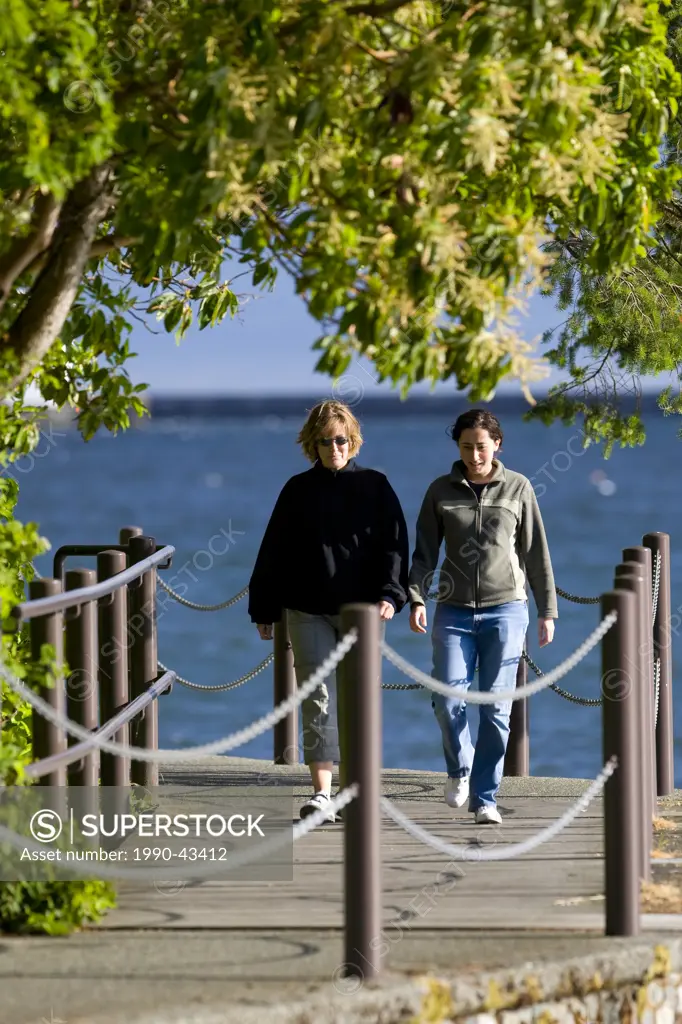 Two women engaged in conversation, stroll along the songhees walkway in Esquimalt. Victoria, Southern Vancouver Island, British Columbia, Canada.