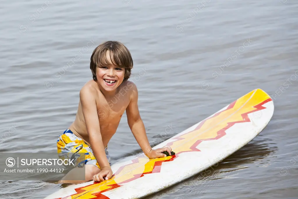Young happy boy playing in water on a surfboard. Lake Winnipeg, Gimli, Manitoba, Canada.