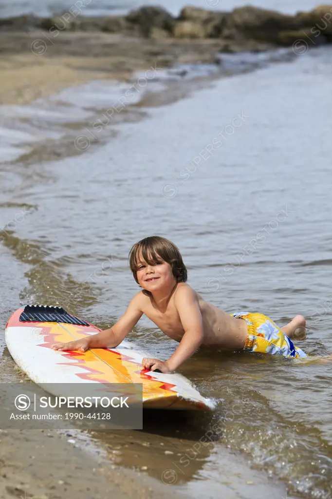 Young smiling boy playing with surfboard on Lake Winnipeg. Gimli, Manitoba, Canada.