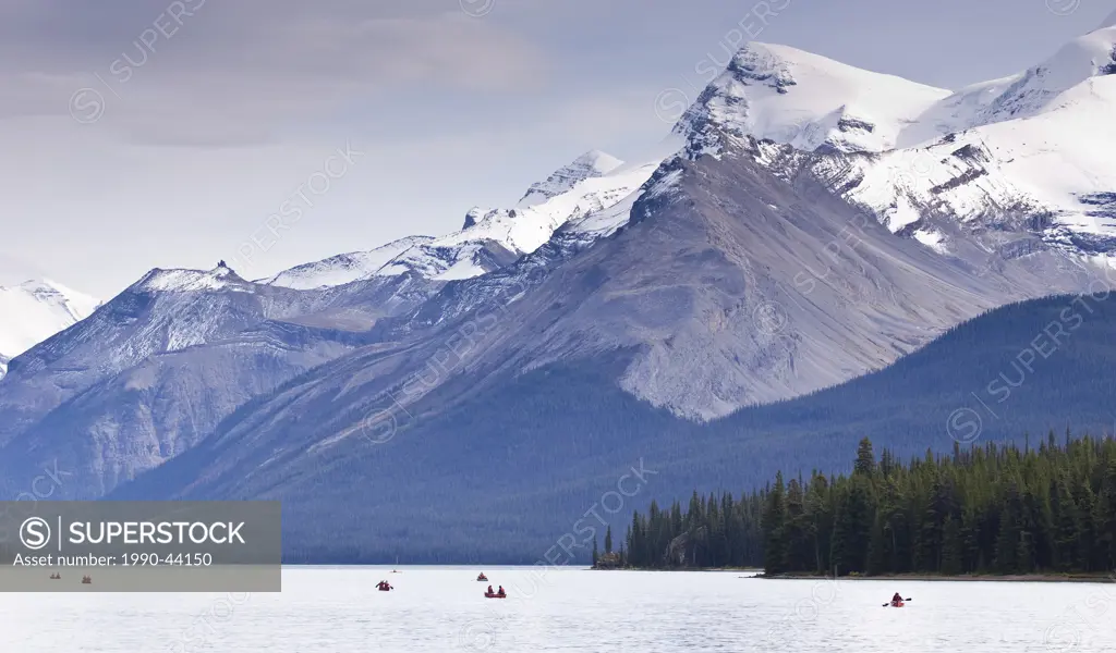 People in small boats and canoes on lake below snow capped mountains, Maligne Lake, Banff National Park, Alberta, Canada