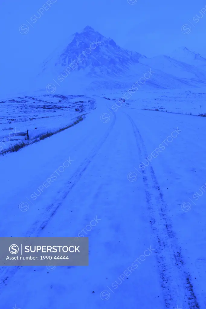 The Dempster Highway leads towards Angelcomb Peak as it is enshrouded by blowing snow, Yukon Territory, Canada.