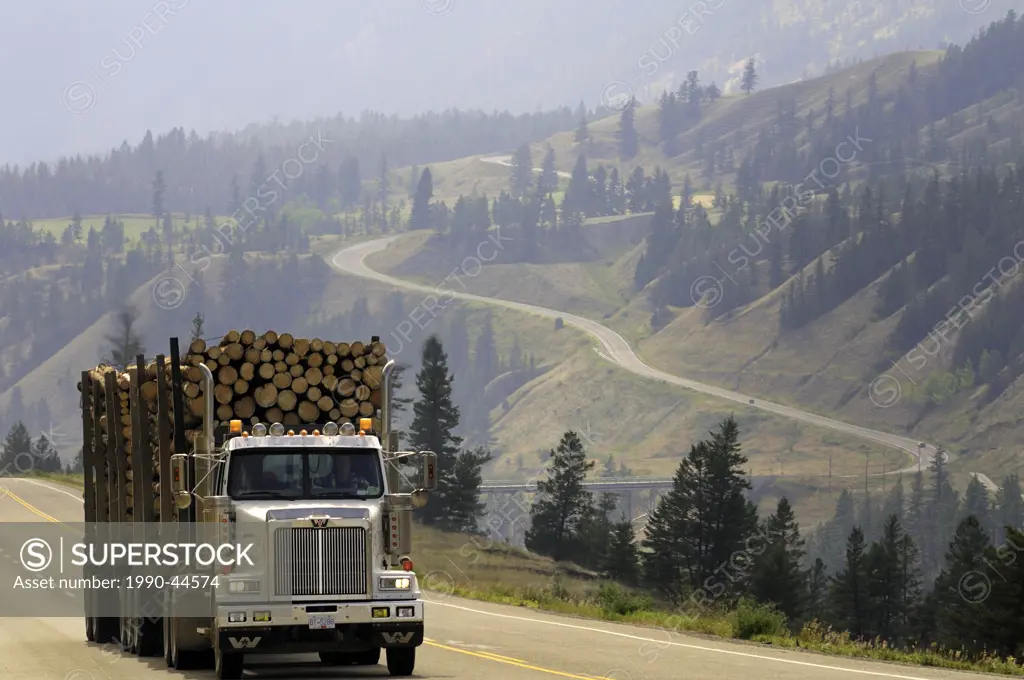 Logging truck loaded with logs, lingering forest fire smoke in the background, Highway 20, Cariboo Coast Chilcotin Region, British Columbia, Canada.