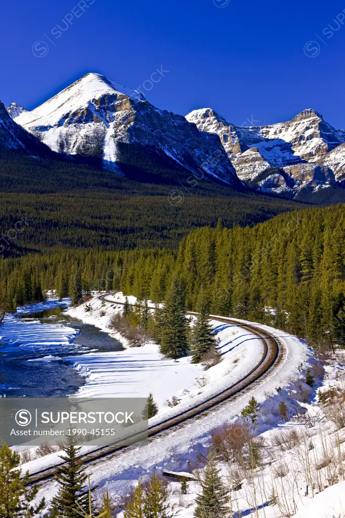 Railway tracks beside the snow and ice fringed Bow River during winter with Fairview Mountain 2743 metres/9001 feet in the background, Banff National ...