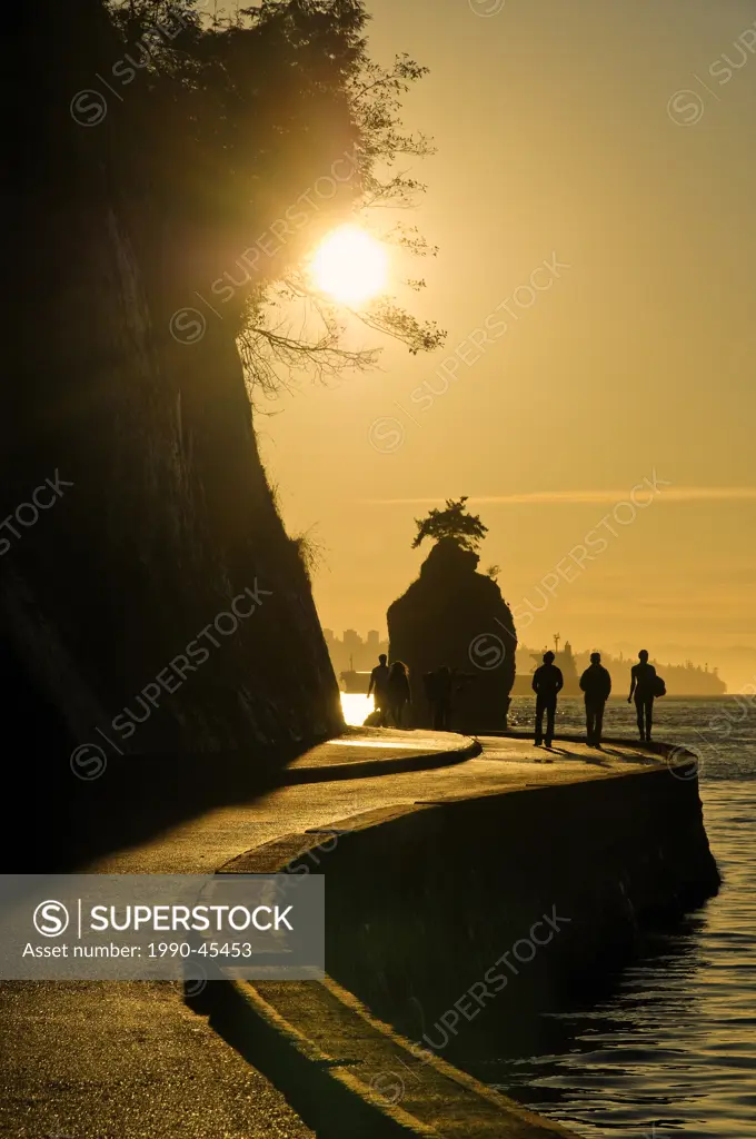 Sunset silhouettes Siwash Rock, with people on the Stanley Park seawall, Vancouver, British Columbia Canada