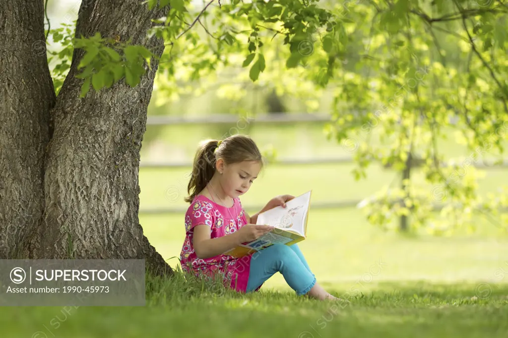 Younge girl reading a book under a tree in Northern Alberta, Canada.