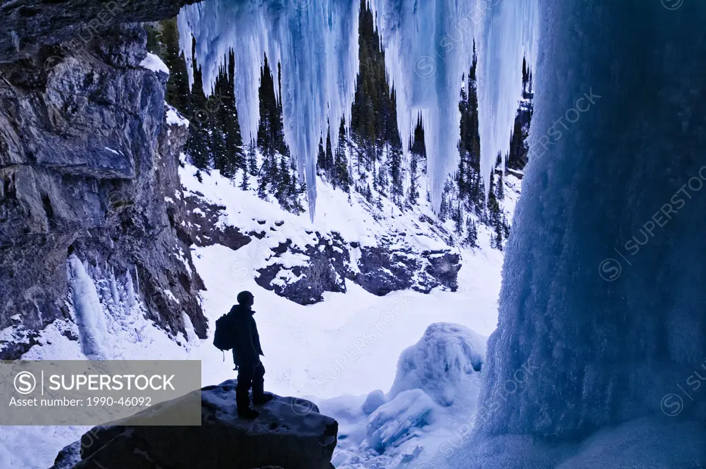 Hiker dwarfed by giant icicles, behind Panther Falls in Winter, Banff National Park, Alberta, Canada