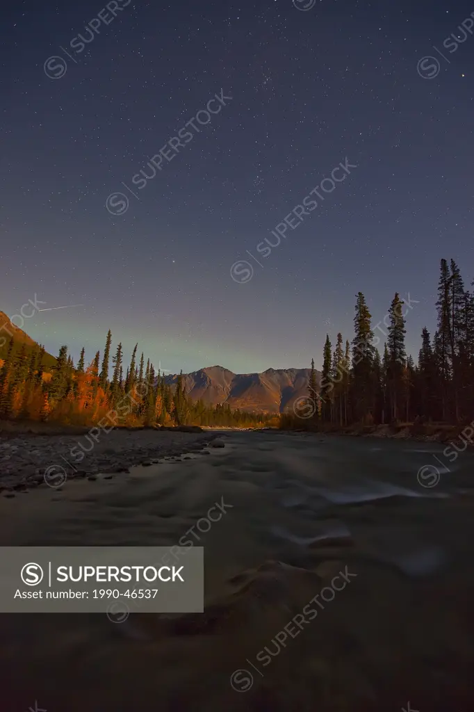 Wheaton River at night with meteor shooting above mountains. Faint aurora seen as well. Yukon, Canada.