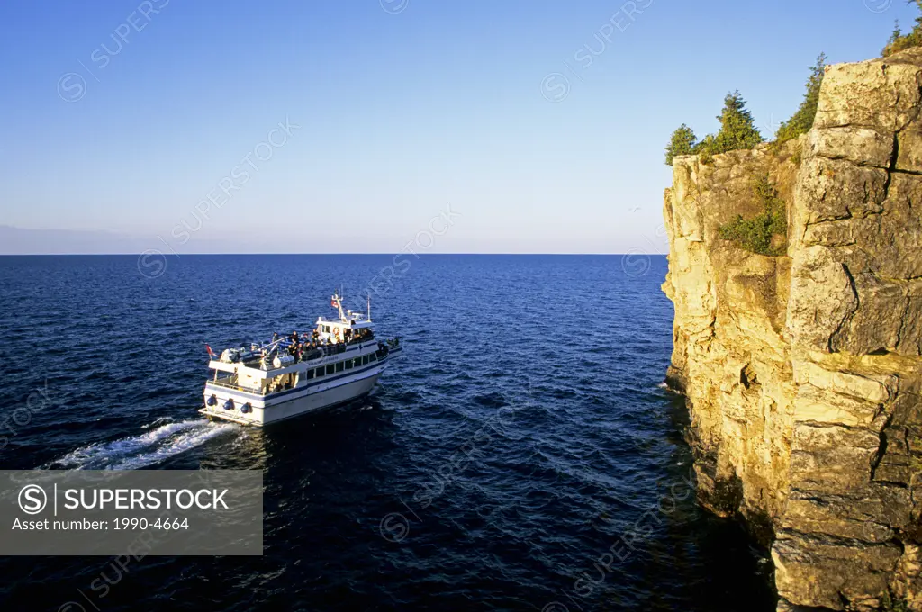 A tour boat heads out for a sunset cruise on Georgian Bay along the cliffs of the Niagara Escarpment in Bruce Peninsula National Park, Ontario, Canada