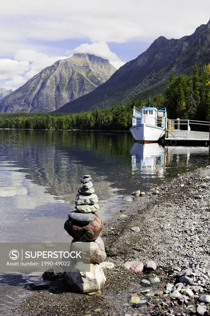An inukshuk sits on the shoreline while tour boat DeSmet is docked on Lake McDonald, Glacier National Park, Montana, United States of America